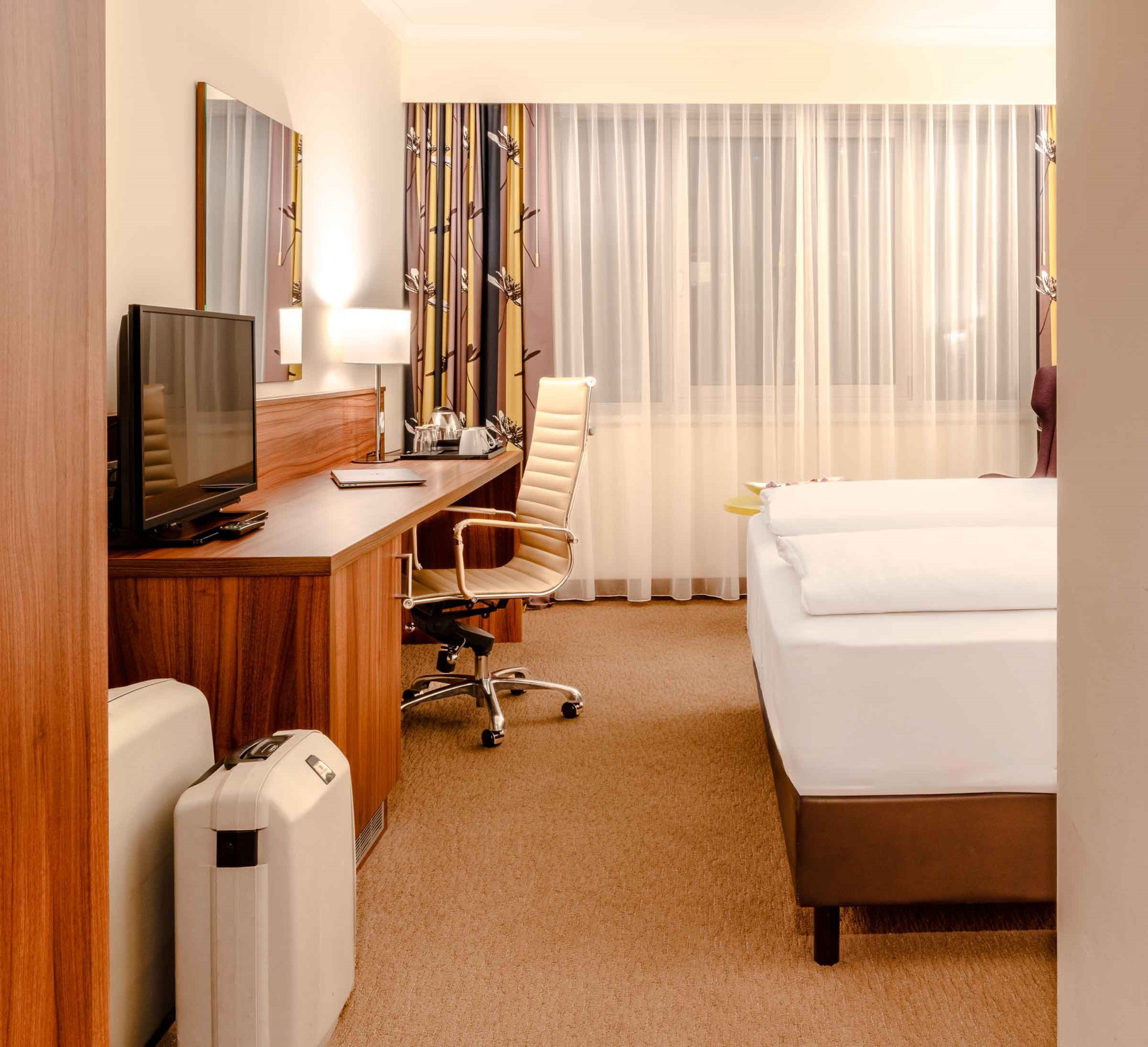 A hotel room with a bed, desk, chair, television, and curtains.