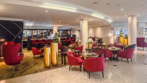 A modern hotel lobby with red chairs, a bar area, and large decorative vases. - PLAZA Premium Wien (Vienna)