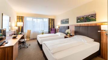 Una habitación de hotel con dos camas, un escritorio con computadora, una silla y un ventanal con cortinas.