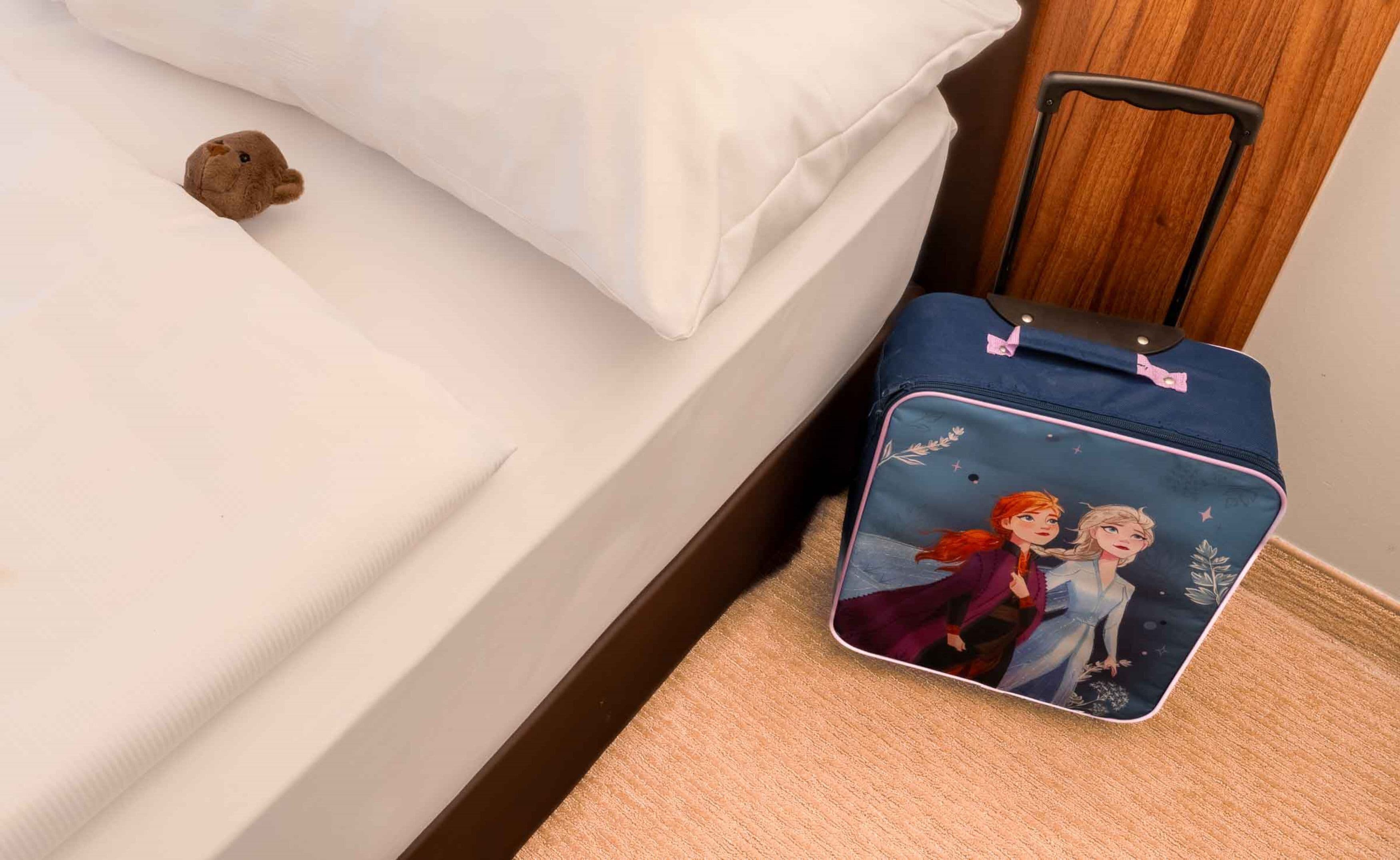 Ein Bett mit einem Kuscheltier und einem Koffer mit einem Motiv aus Die Eiskönigin.