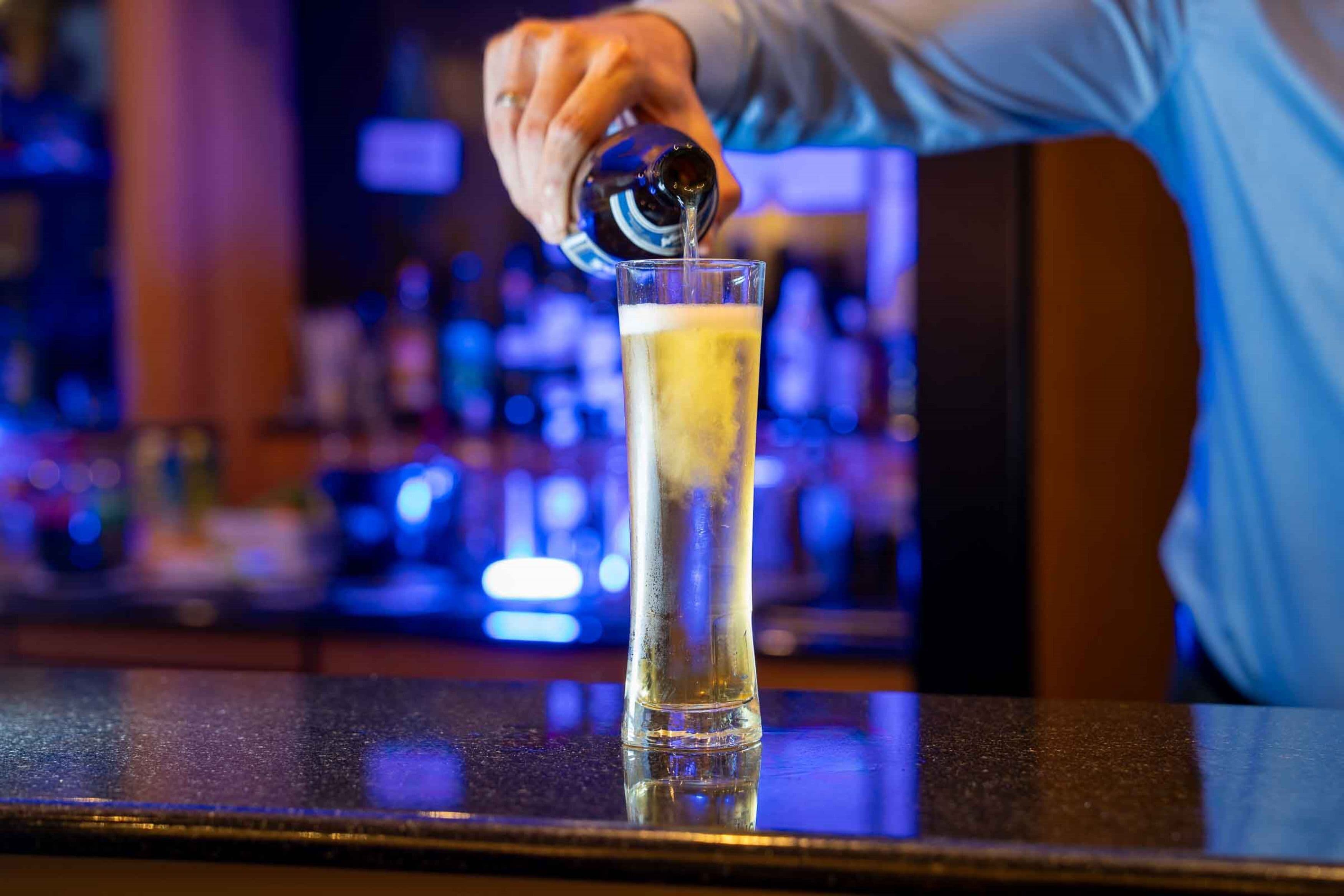 A bartender pouring a drink into a tall glass.