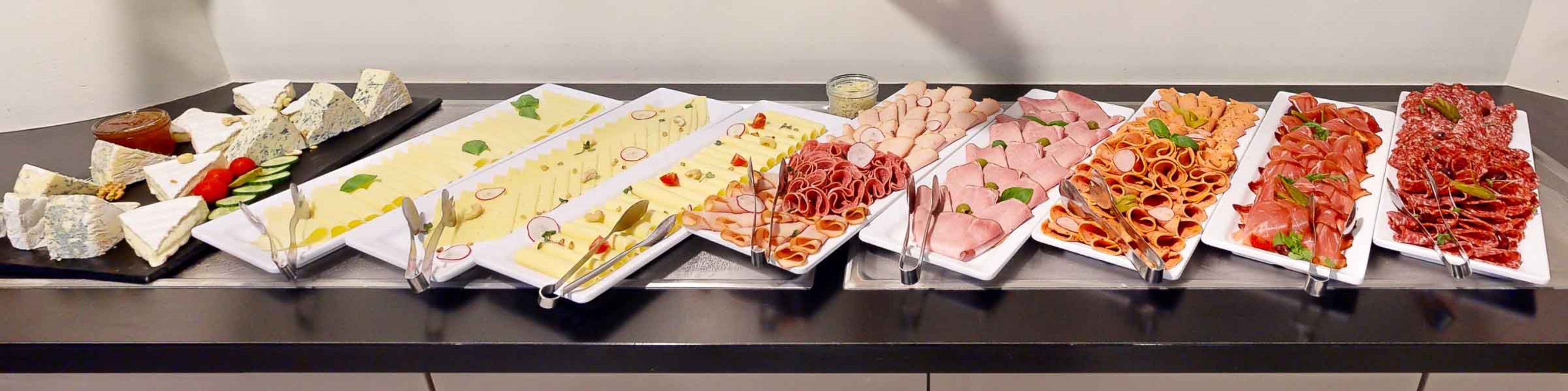 A buffet table with various types of cheeses, meats, and garnishes.
