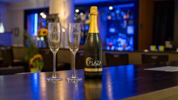 Un'area bar con una bottiglia di champagne Plaza Hotelgroup e due bicchieri vuoti su un bancone.