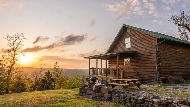 A rustic log cabin with a porch and picnic table, surrounded by a grassy landscape and trees. - The Waterfall Cabin w/ Incredible Sunset View (Ponca)