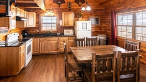 A rustic cabin-style kitchen with wooden cabinets, a wooden dining table, and a refrigerator. - The Waterfall Cabin w/ Incredible Sunset View (Ponca)