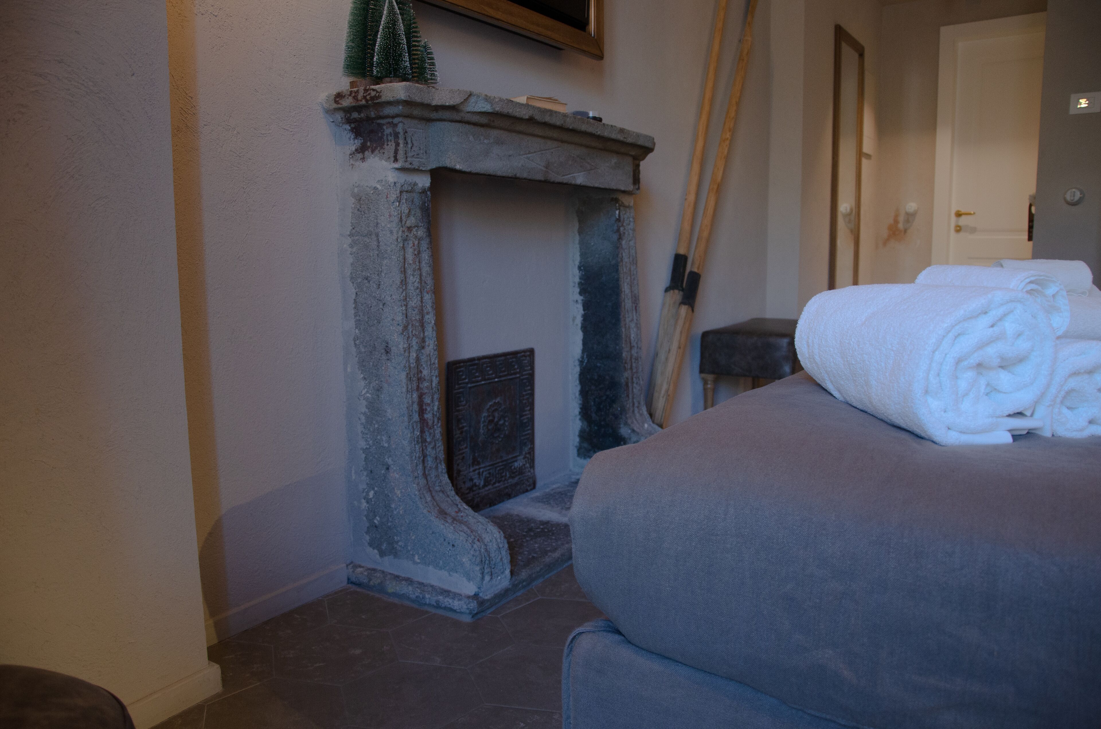 Una habitación con chimenea de piedra, una cama con cubierta gris y una puerta al fondo.
