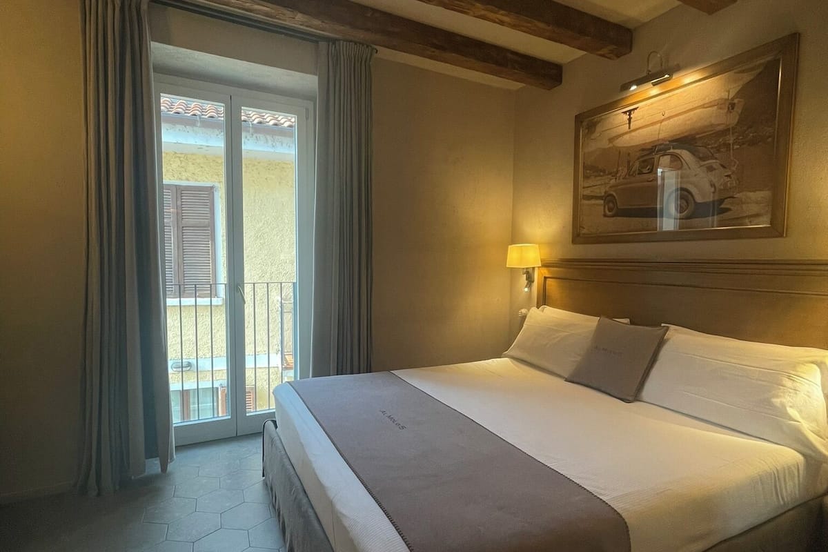 A hotel room with a large bed, a painting on the wall, and a balcony with curtains.