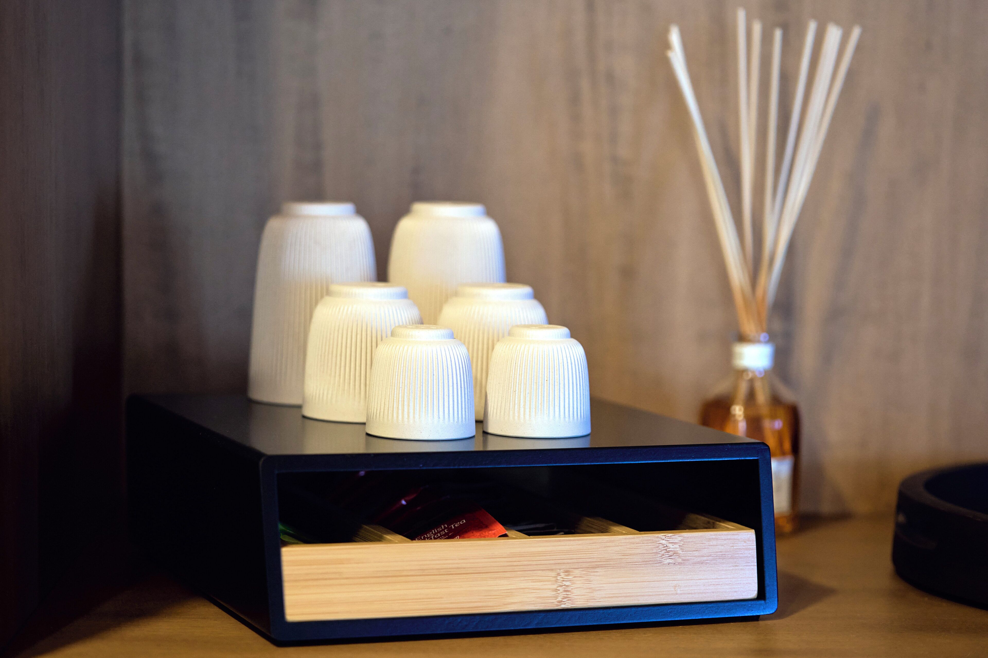 A black storage box with multiple white containers and a bottle of liquid on a wooden surface.