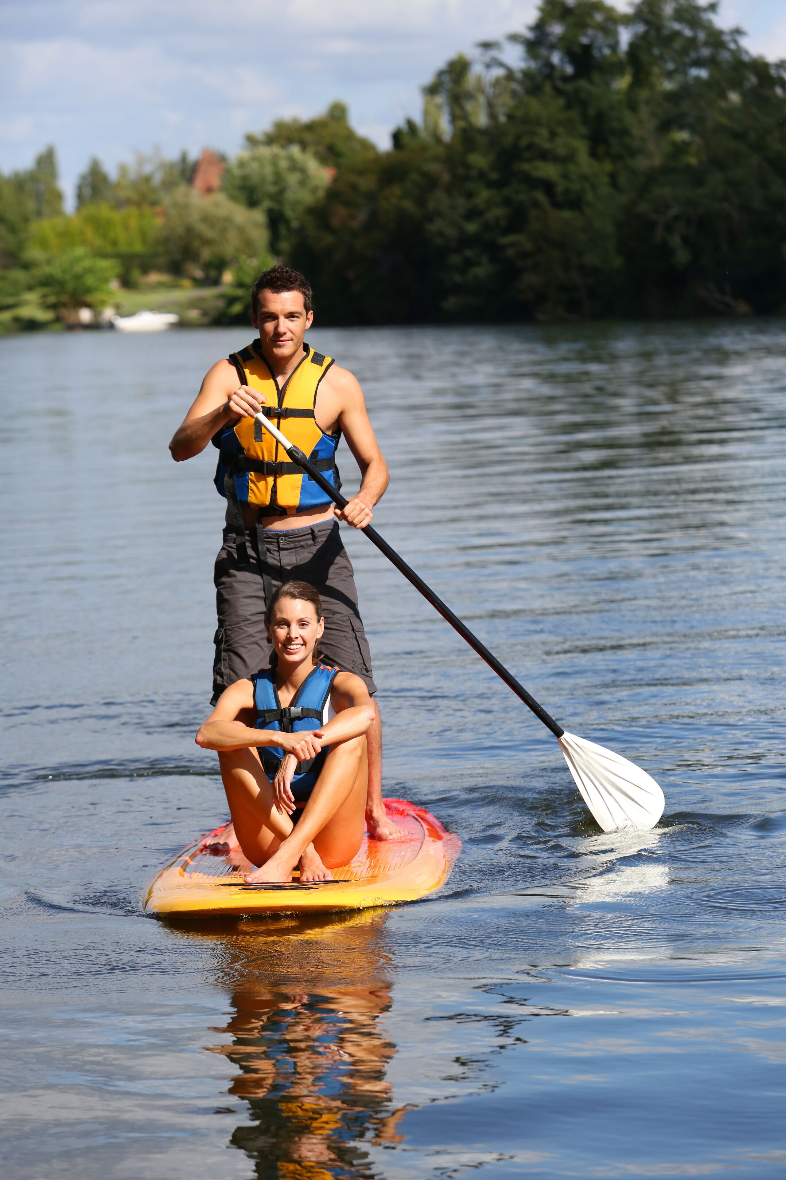 Two people on a paddleboard in a calm body of water, surrounded by trees.