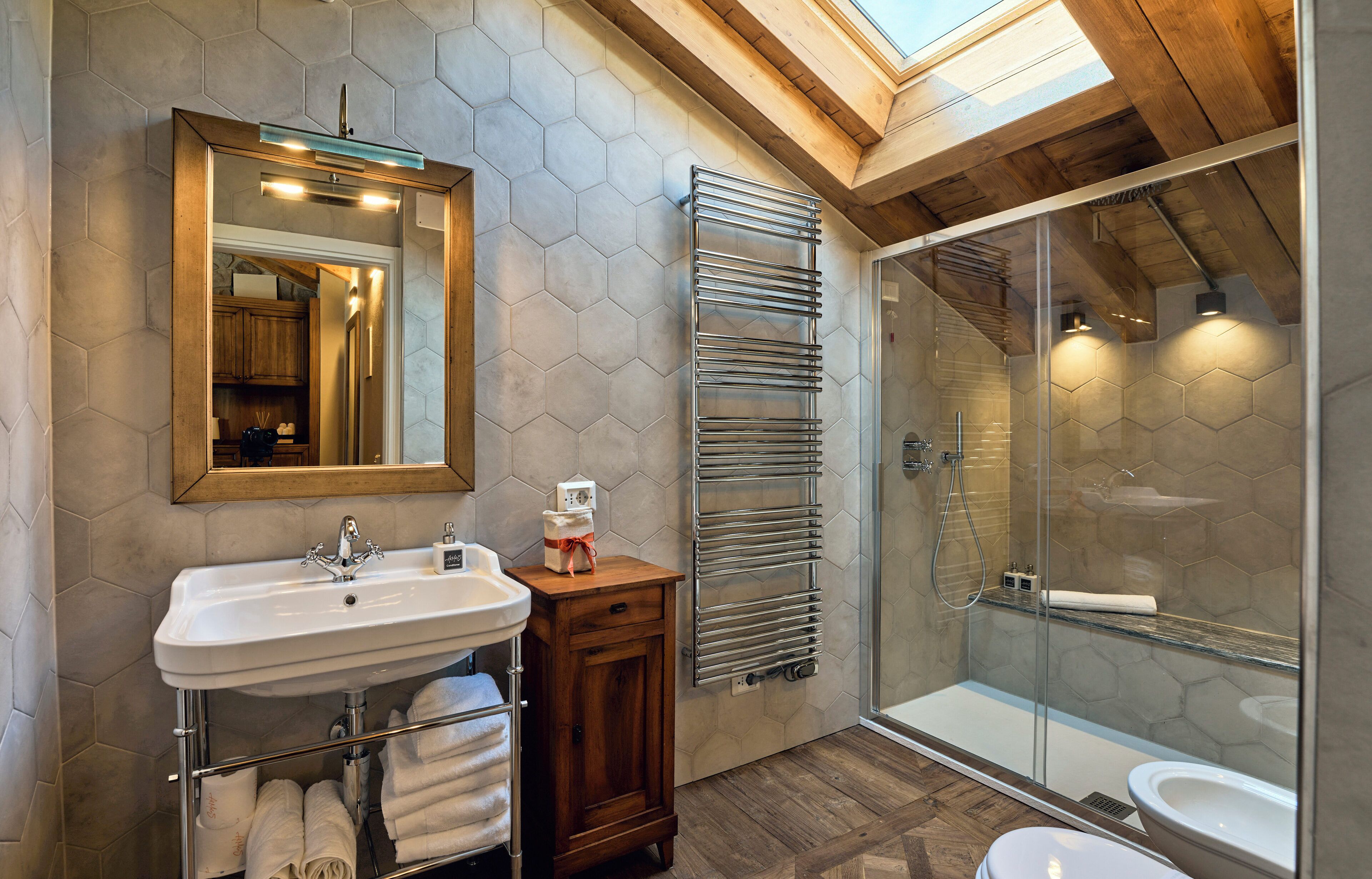 Une salle de bain moderne avec un mur recouvert de carreaux hexagonaux, une douche en verre, un meuble-lavabo en bois et un puits de lumière.