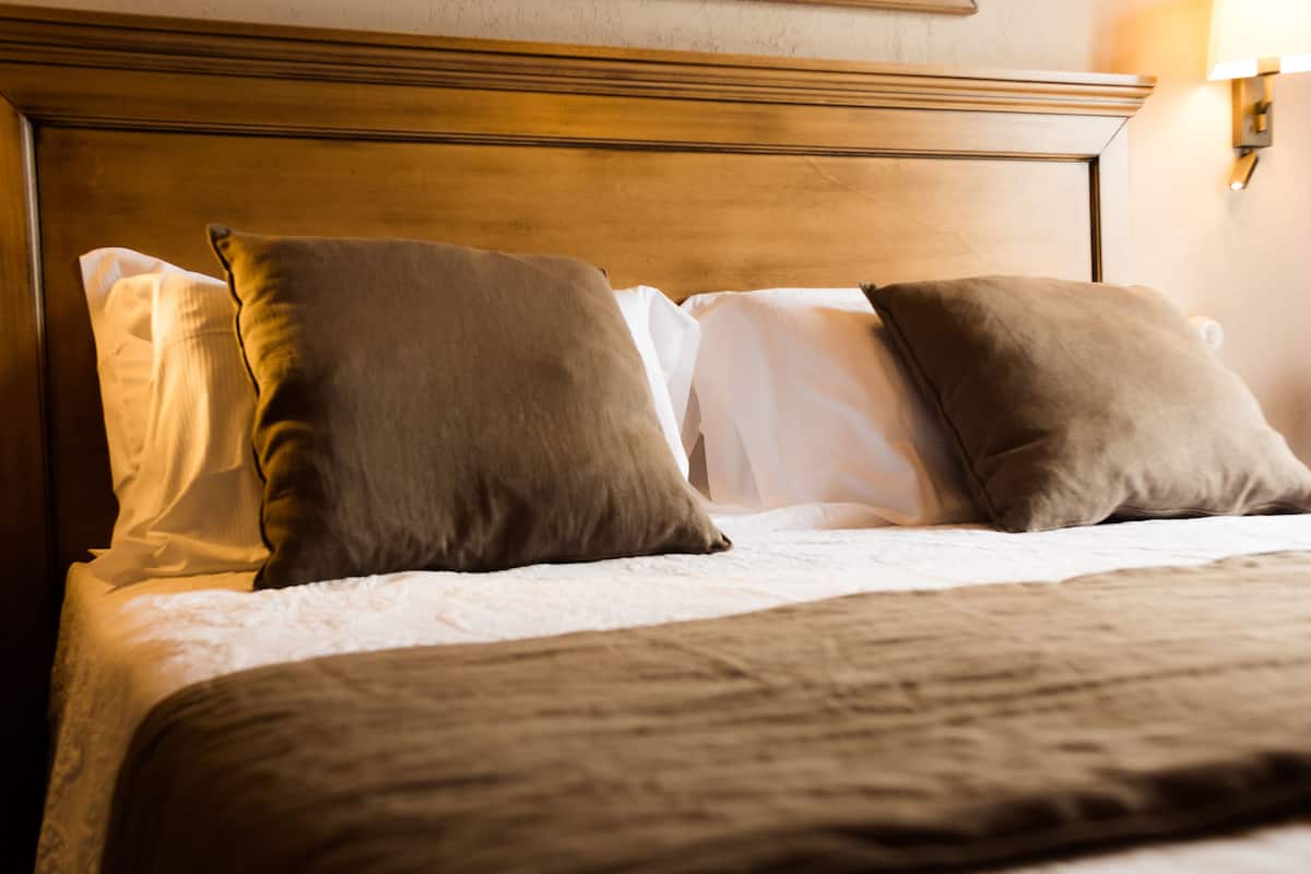 A neatly made bed with a wooden headboard, white linens, and two brown pillows.