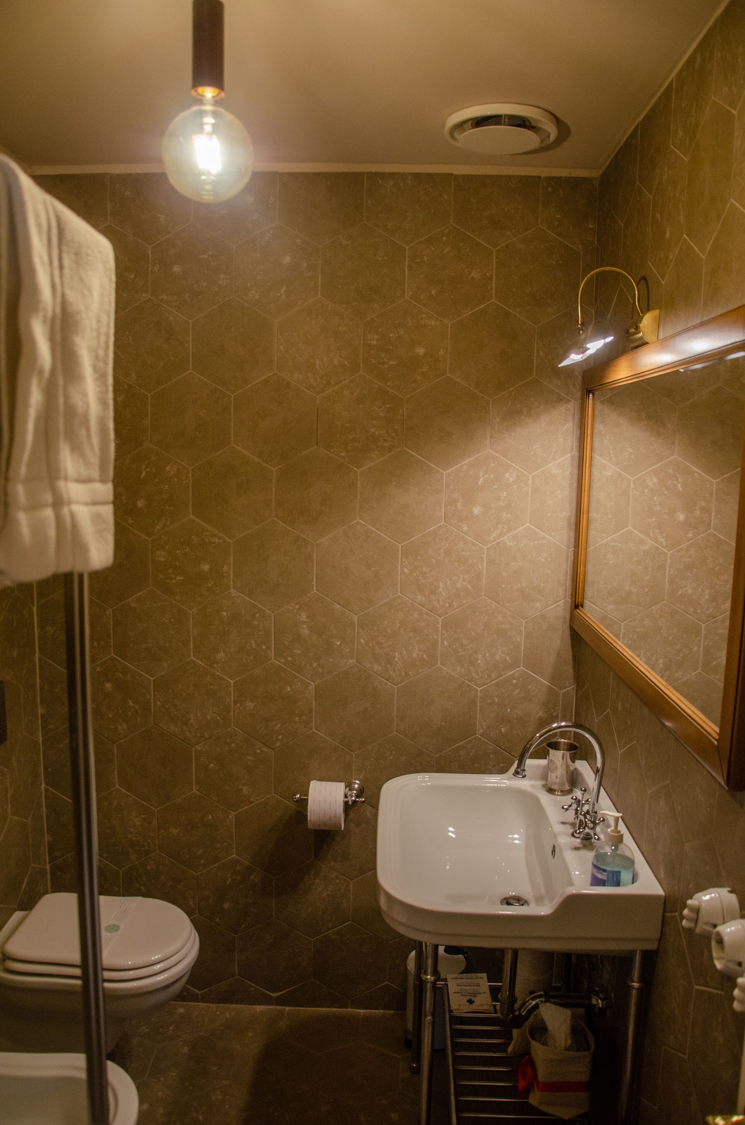 Une salle de bain avec des carreaux hexagonaux, un lavabo blanc, des toilettes et un porte-serviettes.