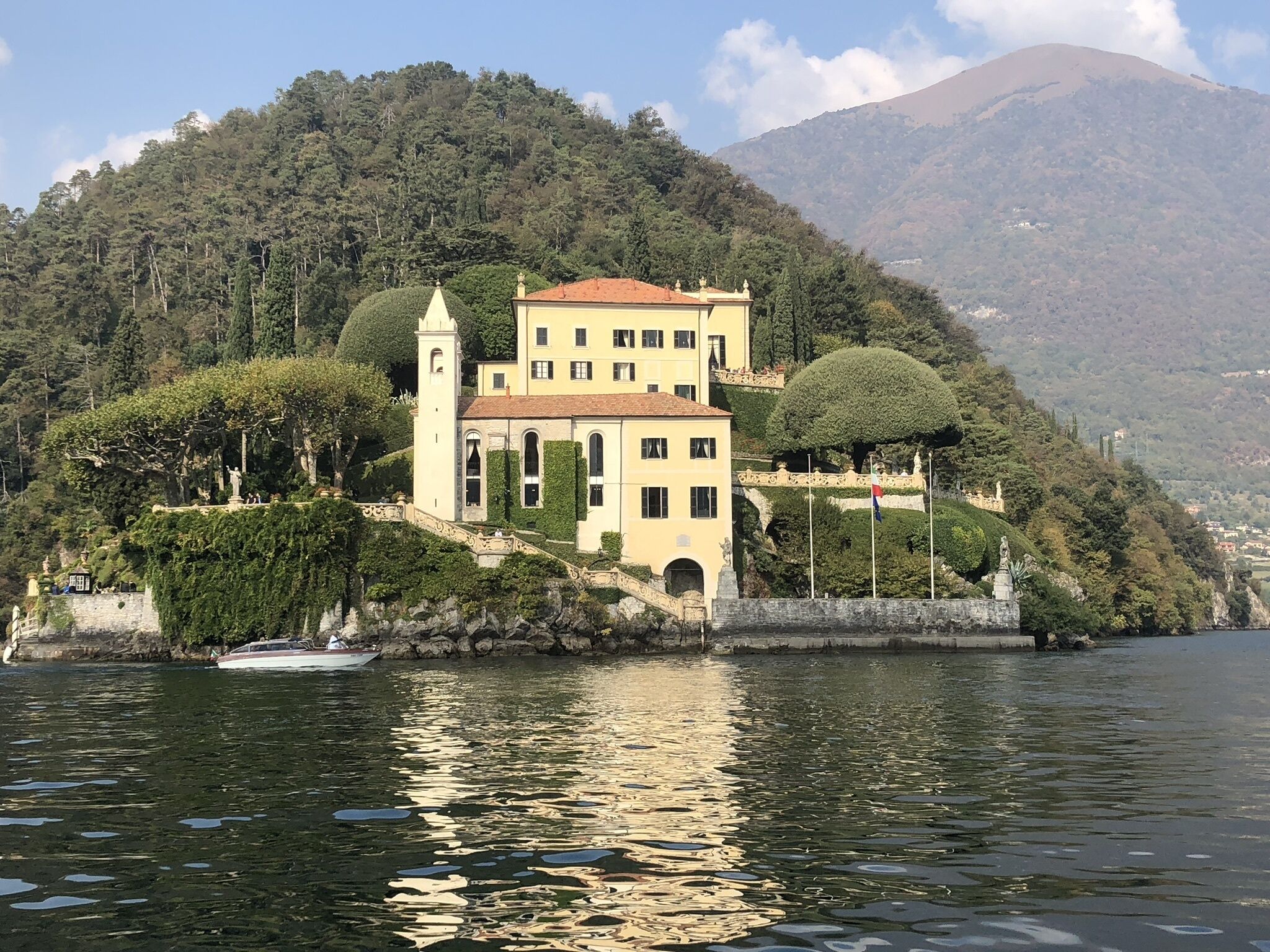 A large, yellow building with a red roof, situated on a hillside by a body of water.