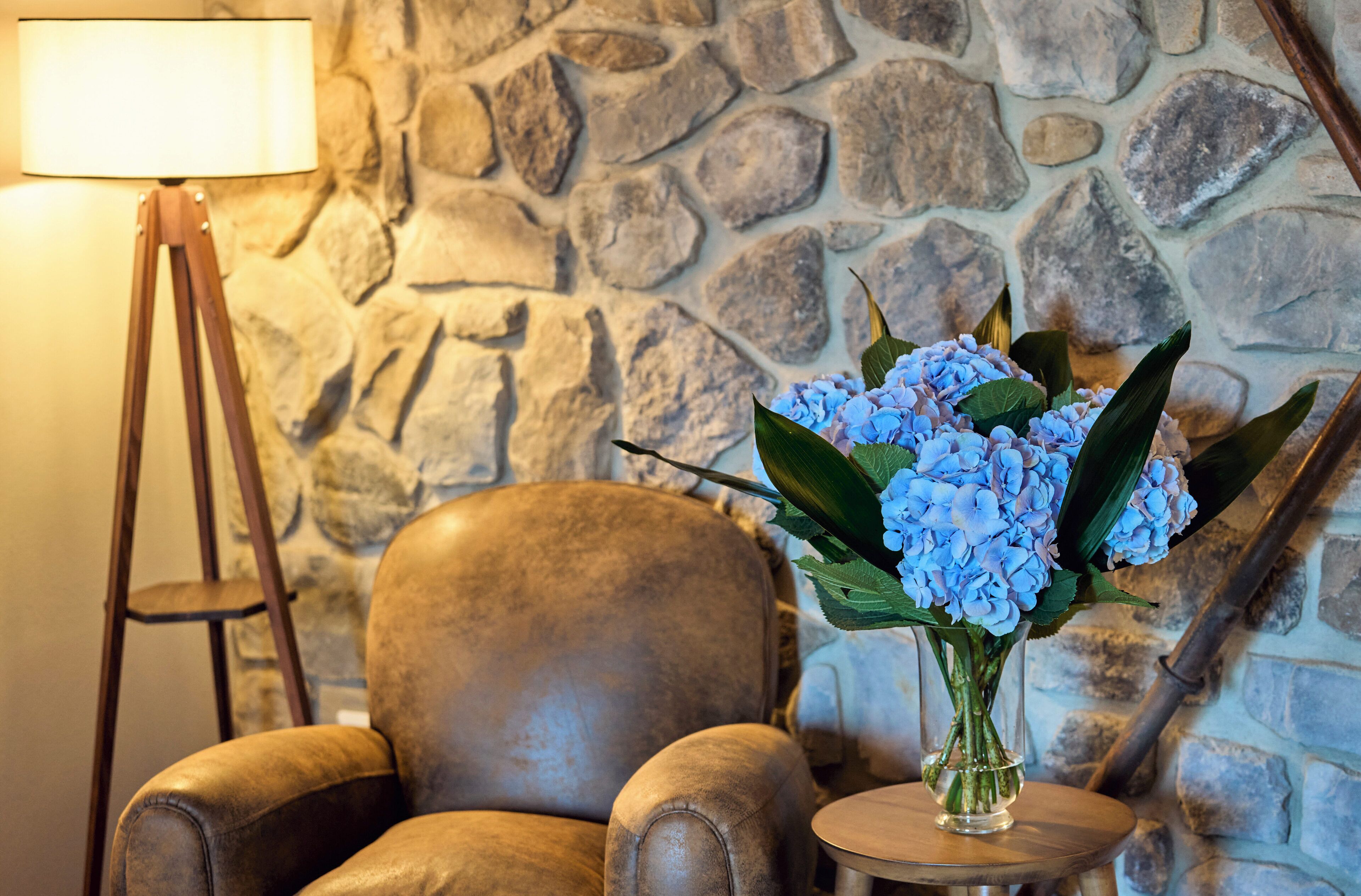 Eine Steinsäule, ein Ledersessel, ein kleiner Tisch mit Blumen in einer Vase und eine Stehlampe.