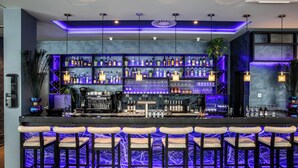 A bar area with multiple shelves of bottles and glasses, a counter with bar equipment, and several bar stools. - NYX Hotel Hamburg by Leonardo Hotels (Hamburg)