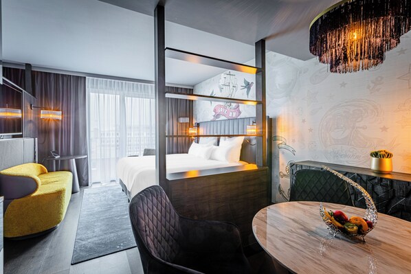 A modern hotel room with a bed, a desk, a dining area, and a view of the city. - NYX Hotel Hamburg by Leonardo Hotels (Hamburg)
