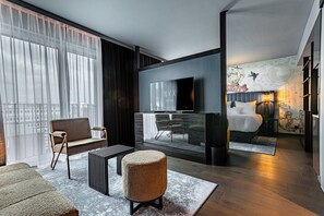 A modern hotel room with a large window, a flat-screen TV, a bed, and a seating area with a chair and ottoman. - NYX Hotel Hamburg by Leonardo Hotels (Hamburg)