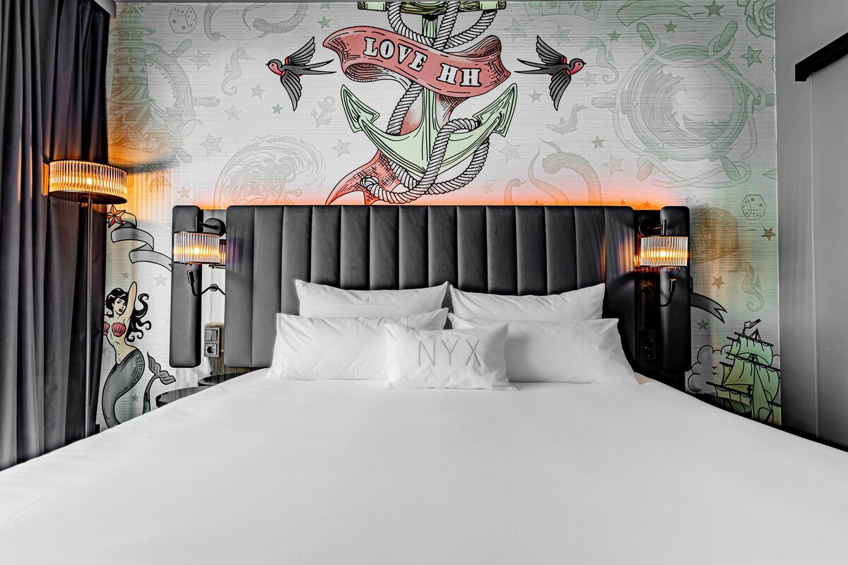 A bed with white bedding, a black upholstered headboard, and two wall-mounted lamps.