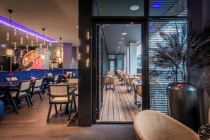 A modern restaurant with a blue seating area, wooden tables, and a large decorative wall. - NYX Hotel Hamburg by Leonardo Hotels (Hamburg)