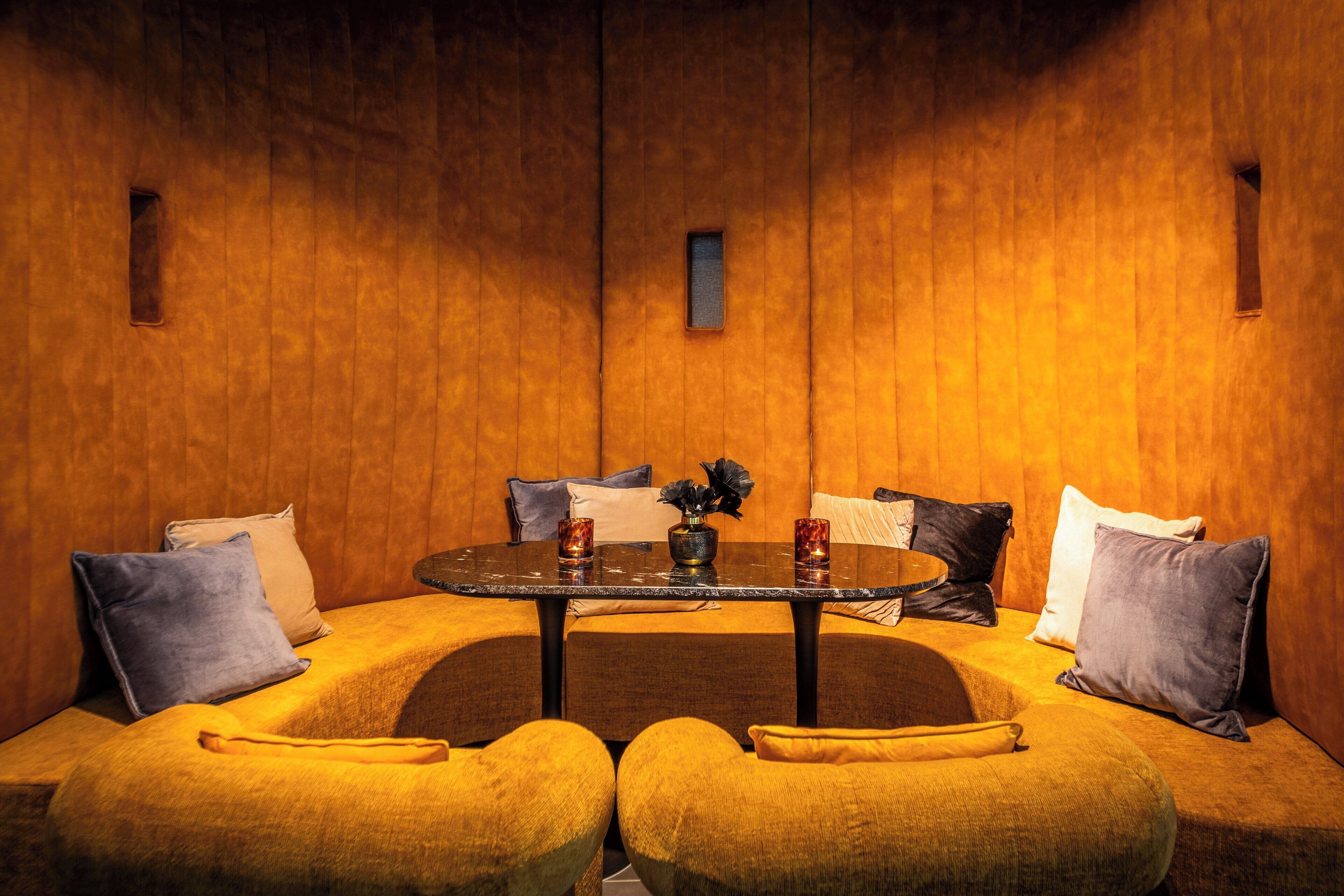 A cozy room with a round table, yellow upholstered seating, and a wooden wall.