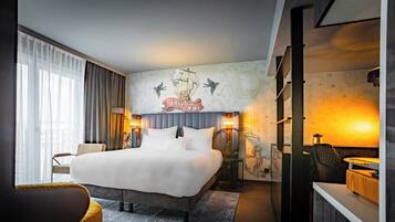 Ein modernes Hotelzimmer mit einem großen Bett, einem Schreibtisch und einem Stuhl. Ein Fenster mit Vorhängen und eine Wand mit einem dekorativen Wandgemälde.