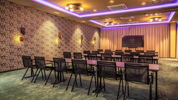 A conference room with a patterned wall, a flat-screen TV, and rows of chairs.