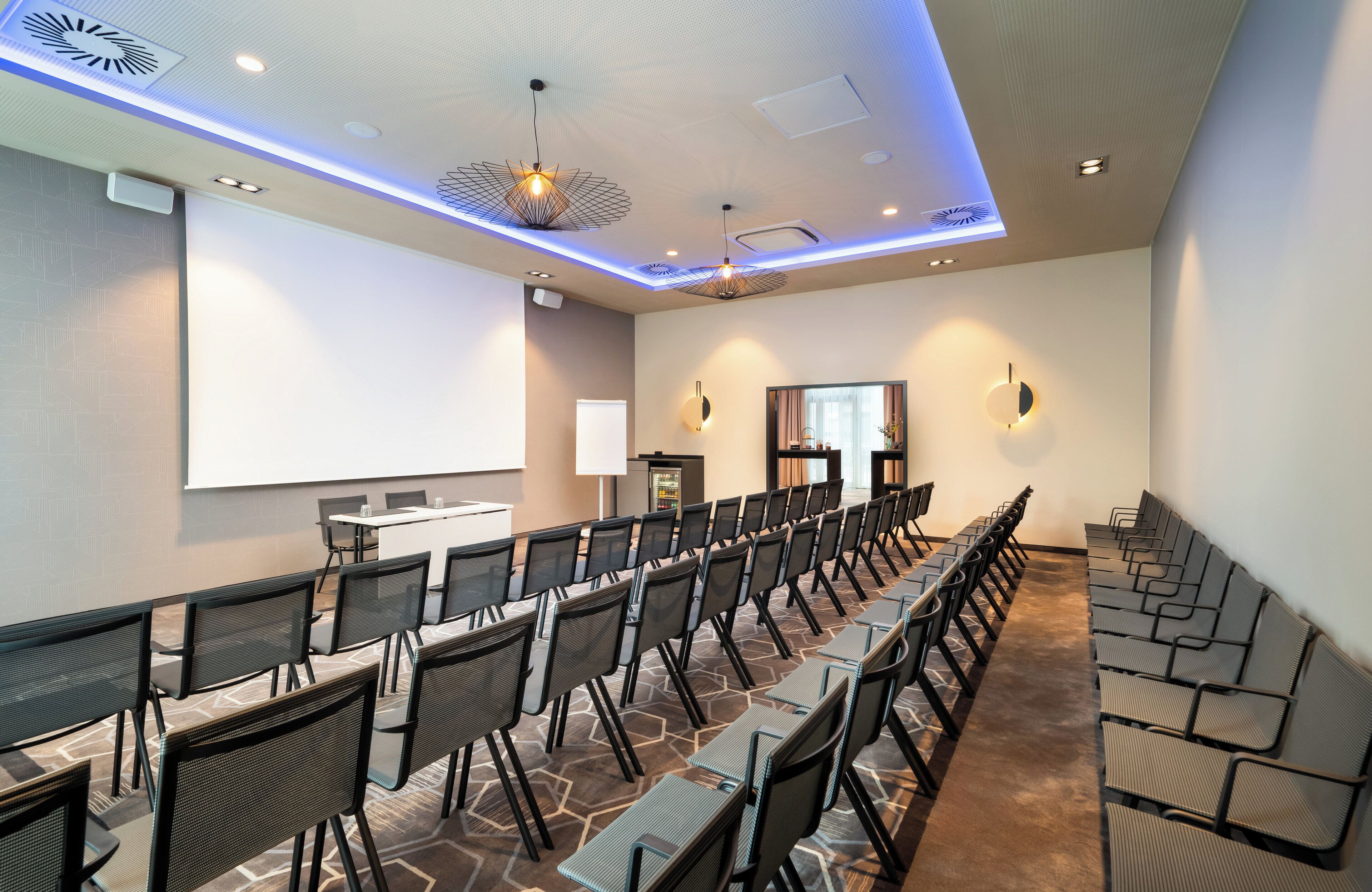 A conference room with rows of chairs, a projector screen, and a presentation area.