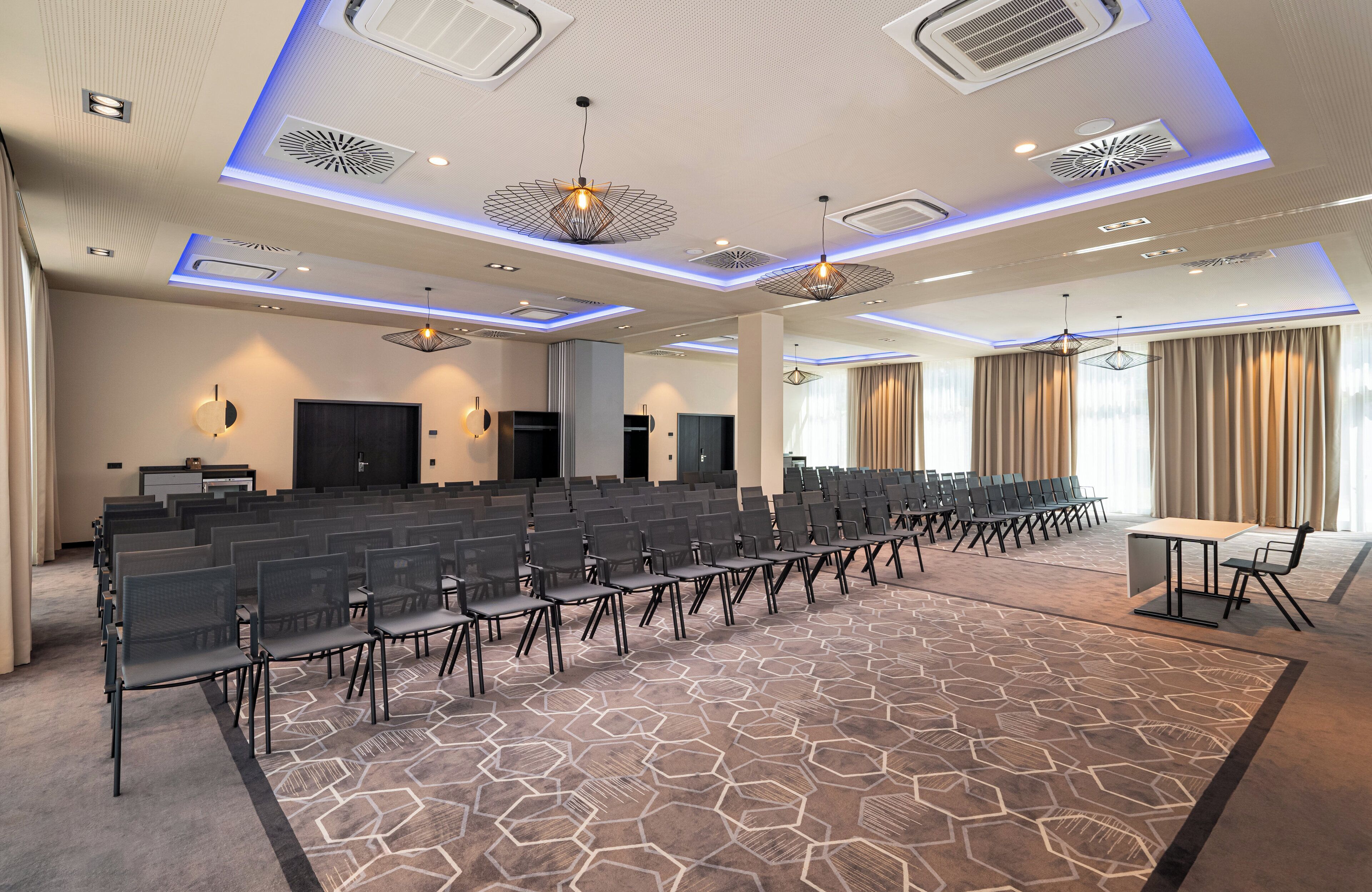 A conference room with rows of chairs, a stage, and a large screen.