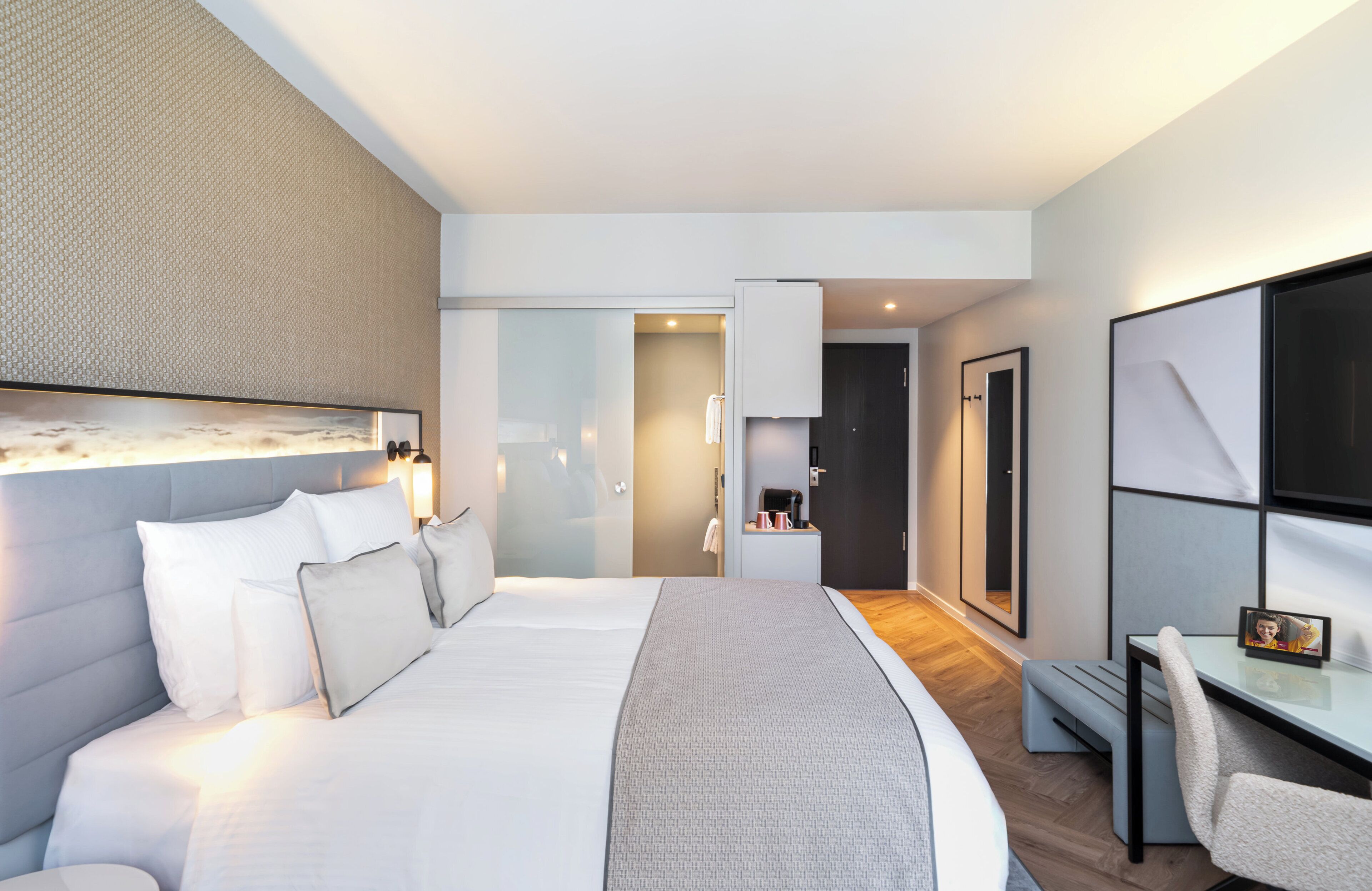 A modern hotel room with a large bed, a desk, and a TV.