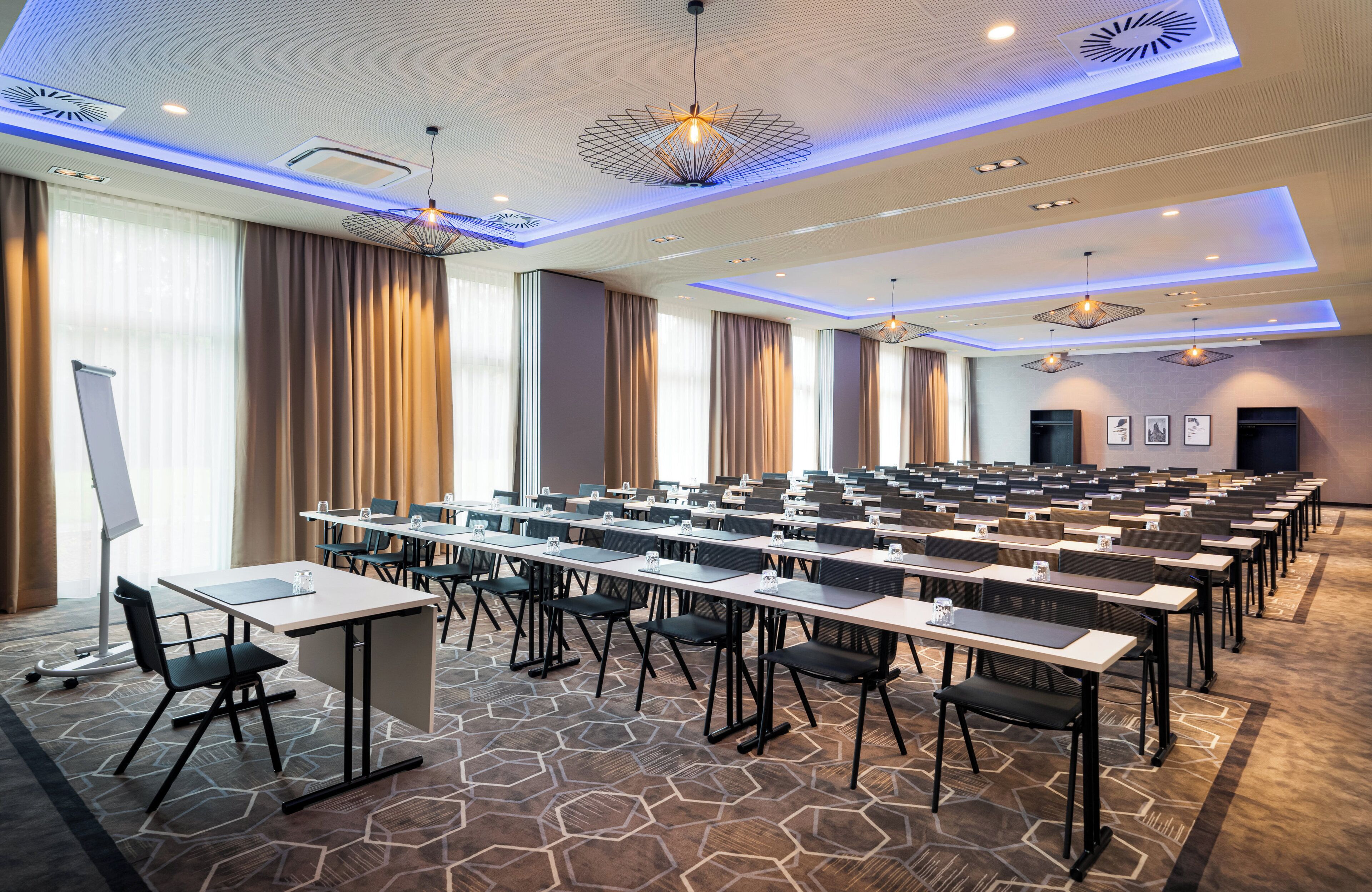 A conference room with rows of tables and chairs, a whiteboard, and a projector stand.