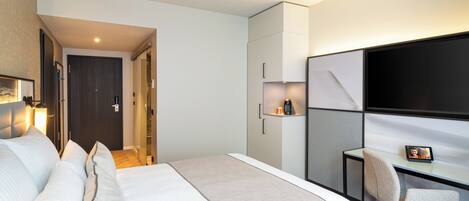 A modern hotel room with a large bed, a desk with a chair, a flat-screen TV, and a wardrobe.