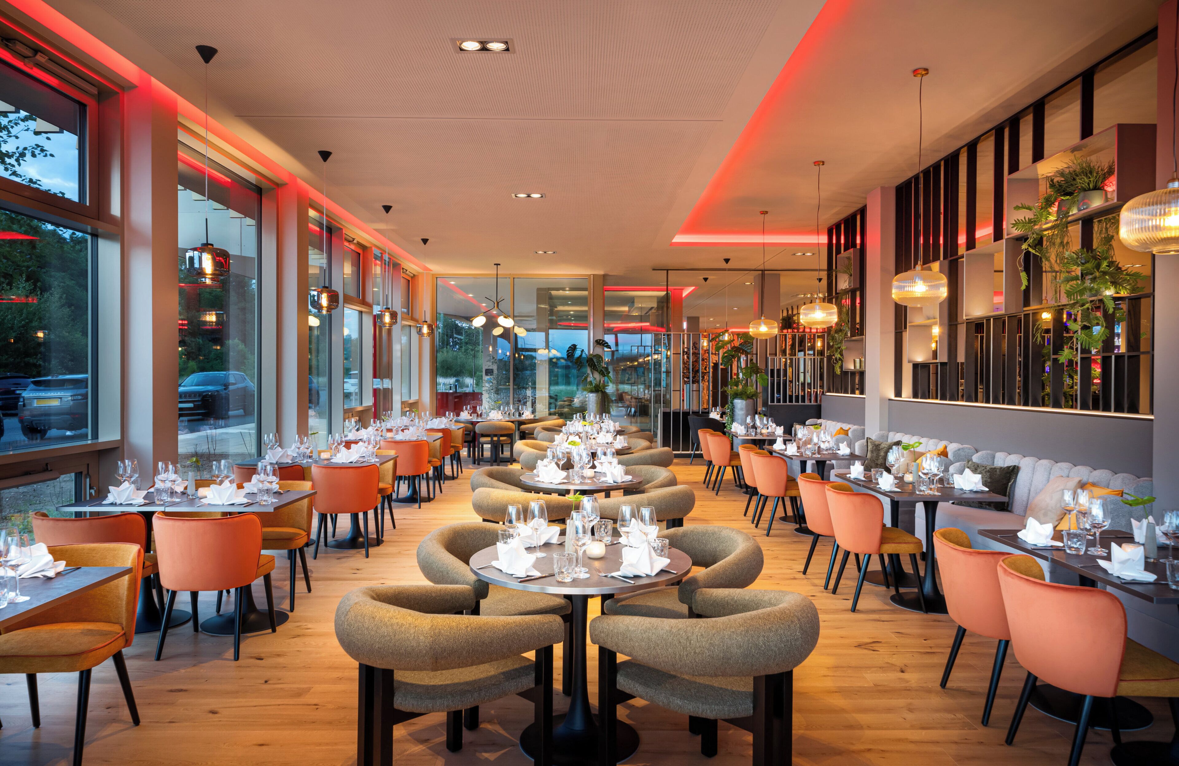 A restaurant interior with round tables, orange chairs, and a view of the street outside.