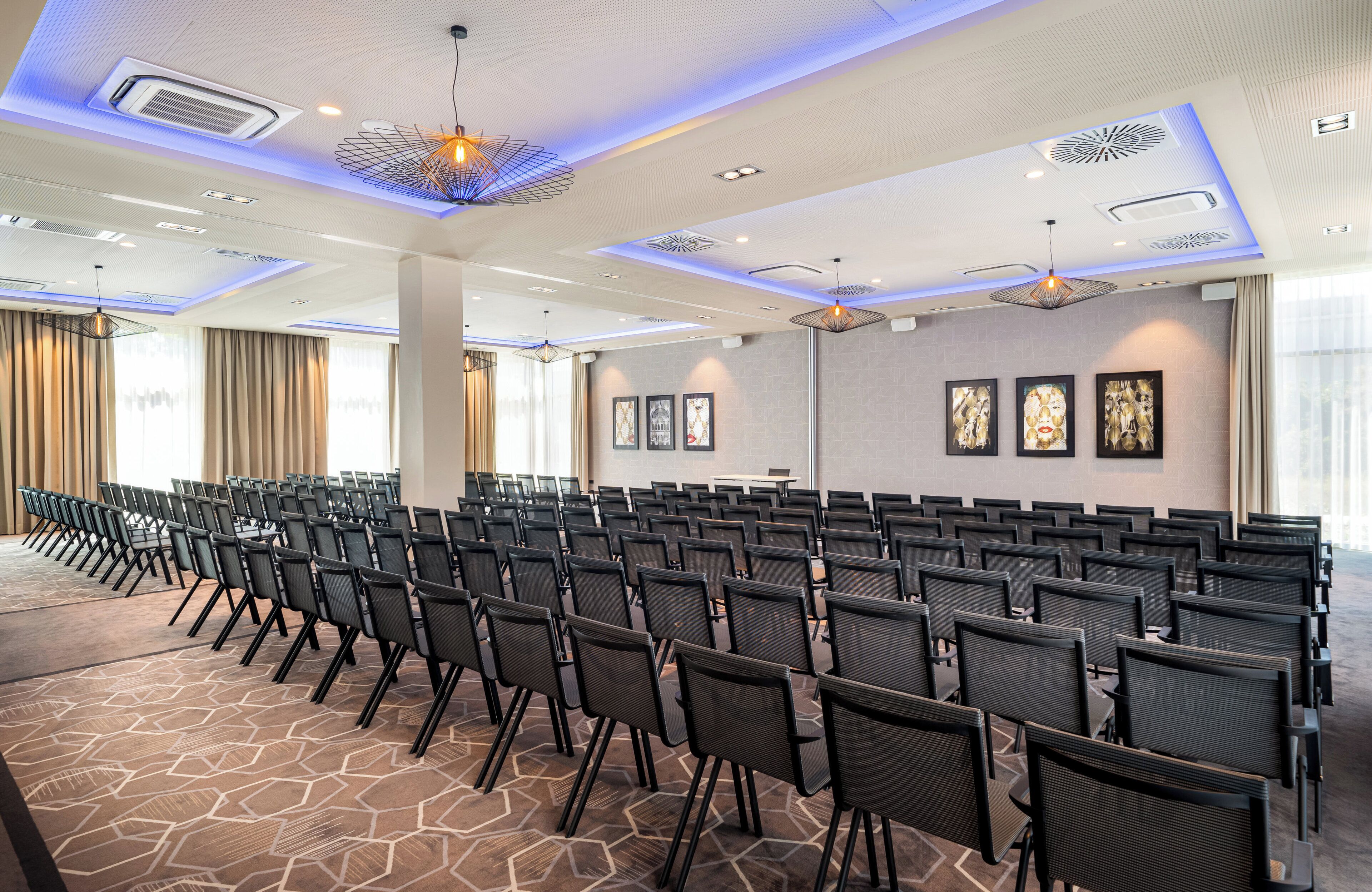 A conference room with rows of chairs, a patterned carpet, and modern lighting fixtures.