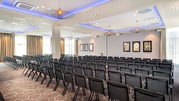 A conference room with rows of chairs, a patterned carpet, and modern lighting fixtures.