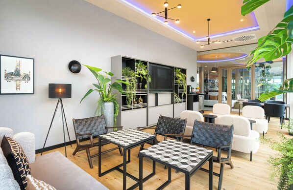 A modern living room with a sofa, two tables, and chairs. There are plants, a TV, and a ceiling light.