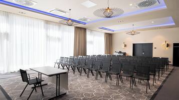Ein Konferenzraum mit einem langen Tisch, Reihen von Stühlen, einem großen Fenster mit Vorhängen und einem modernen Deckendesign.