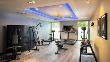 Un gimnasio moderno con diversos equipos de ejercicio, techo con iluminación azul y ventanas amplias.