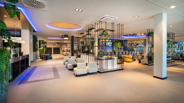 A modern hotel lobby with seating areas, a bar, and decorative plants. - Leonardo Royal Hotel Cologne Bonn Airport (Cologne)