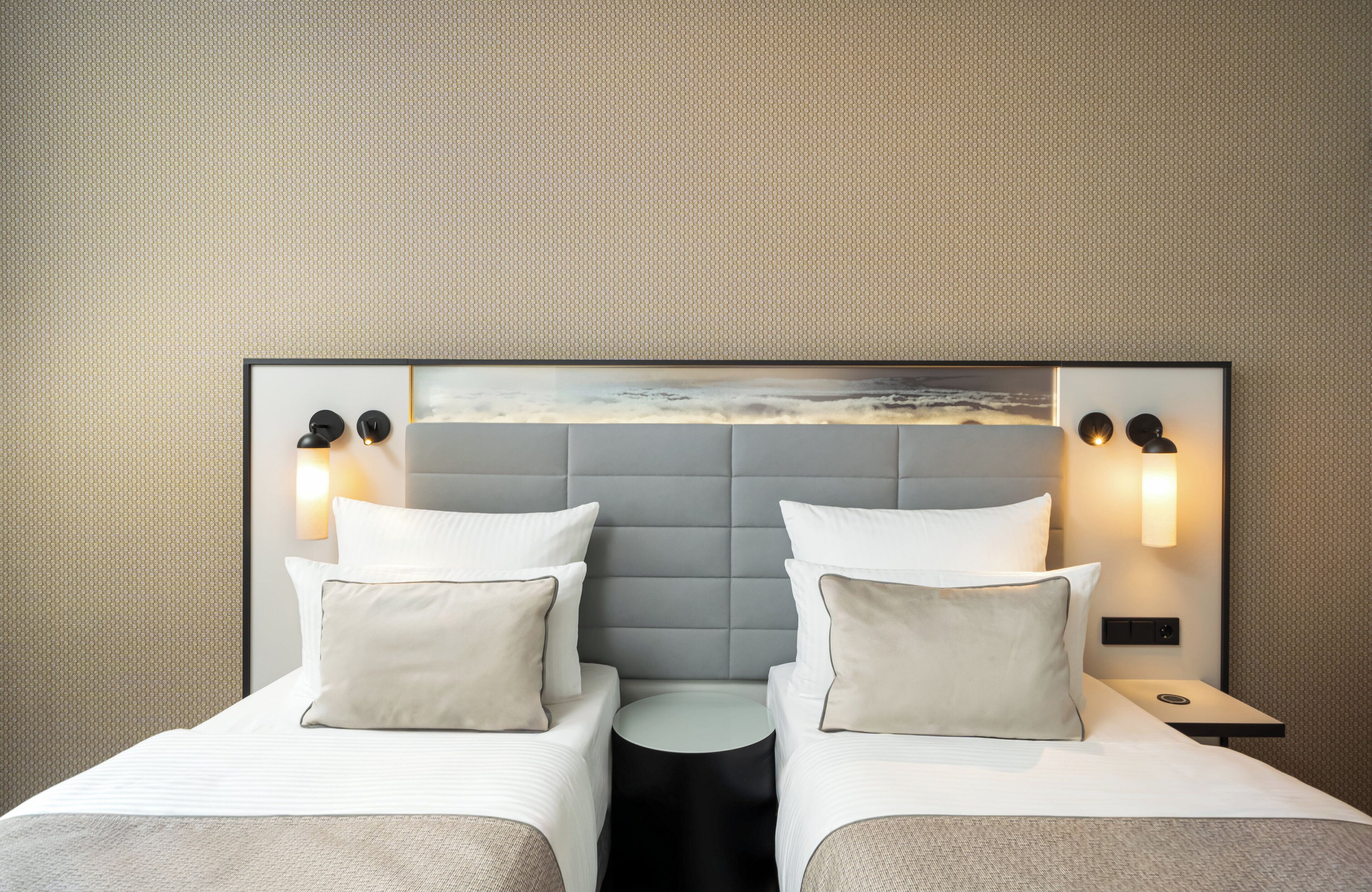 A hotel room with a large bed, two bedside tables, and a headboard with a landscape painting.