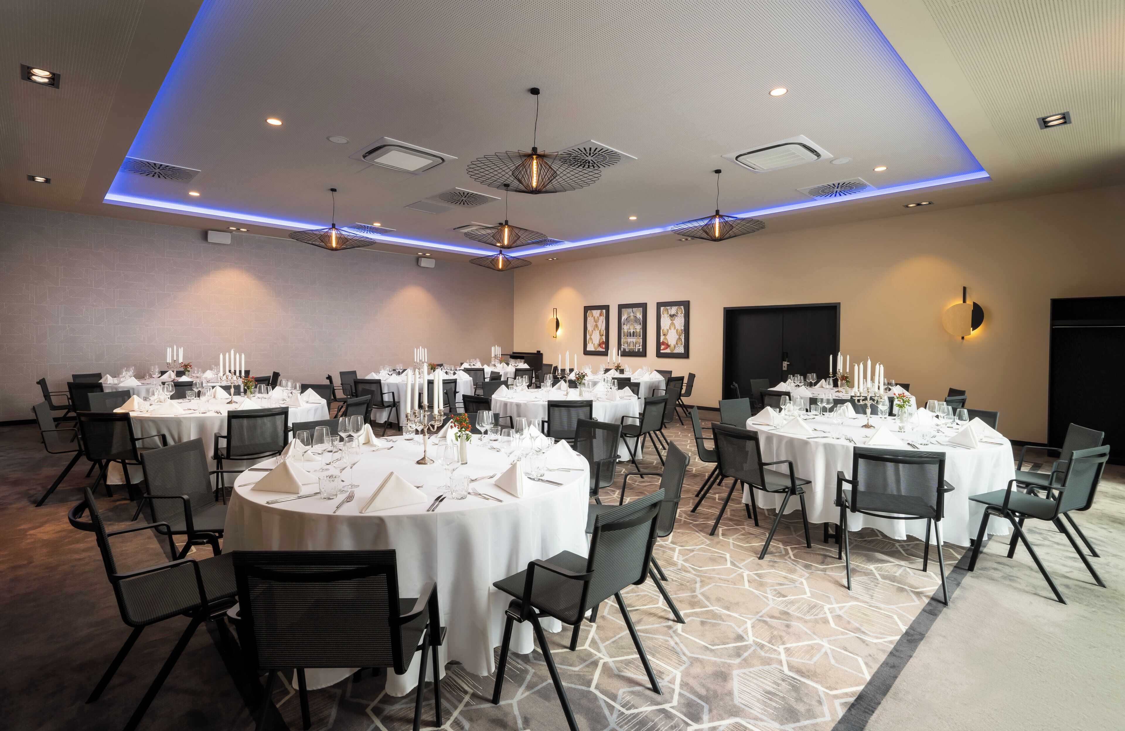 A banquet hall with round tables set for dining, black chairs, and a patterned carpet.