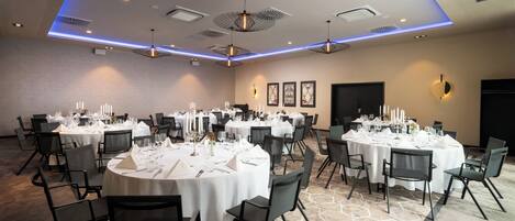 A banquet hall with round tables set for dining, black chairs, and a patterned carpet.