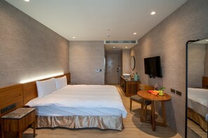 Une chambre d’hôtel avec un grand lit, une table de chevet, une petite table ronde en bois avec une chaise, un petit lavabo et un miroir.