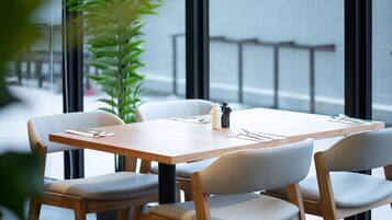 A modern dining area with a wooden table and four chairs, a potted plant, and a view through large windows.