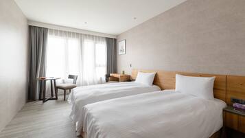 Ein Hotelzimmer mit zwei Betten, einem Schreibtisch, einem Stuhl und einem fensterbelagten Fenster.