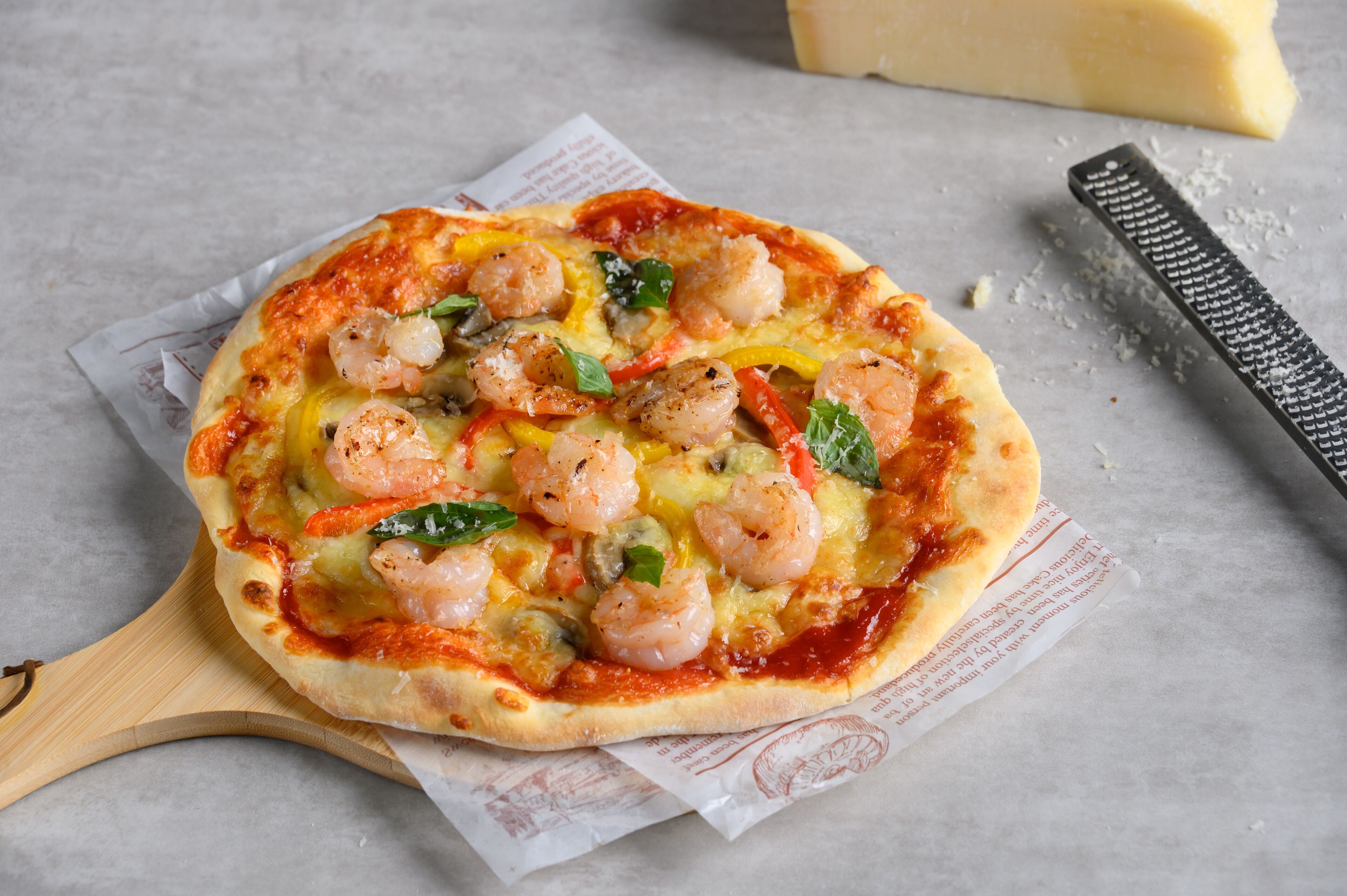 A pizza with shrimp and vegetables on a wooden board.