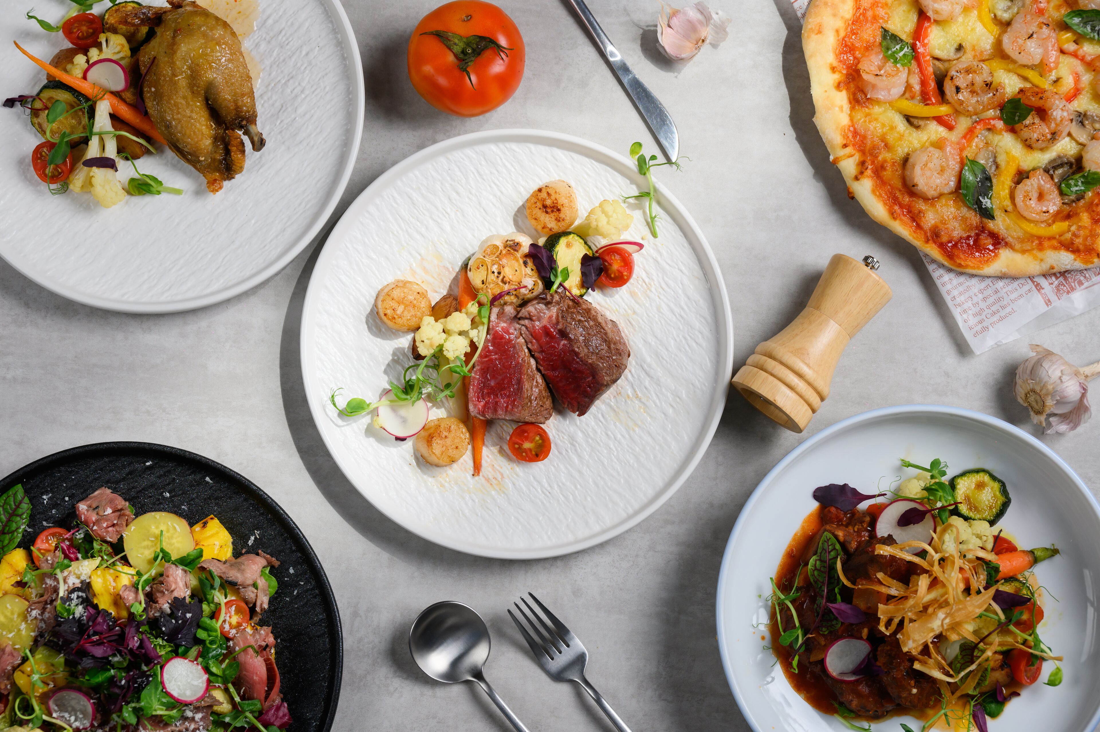 A variety of dishes on plates, including a pizza, a salad, and a meat dish.