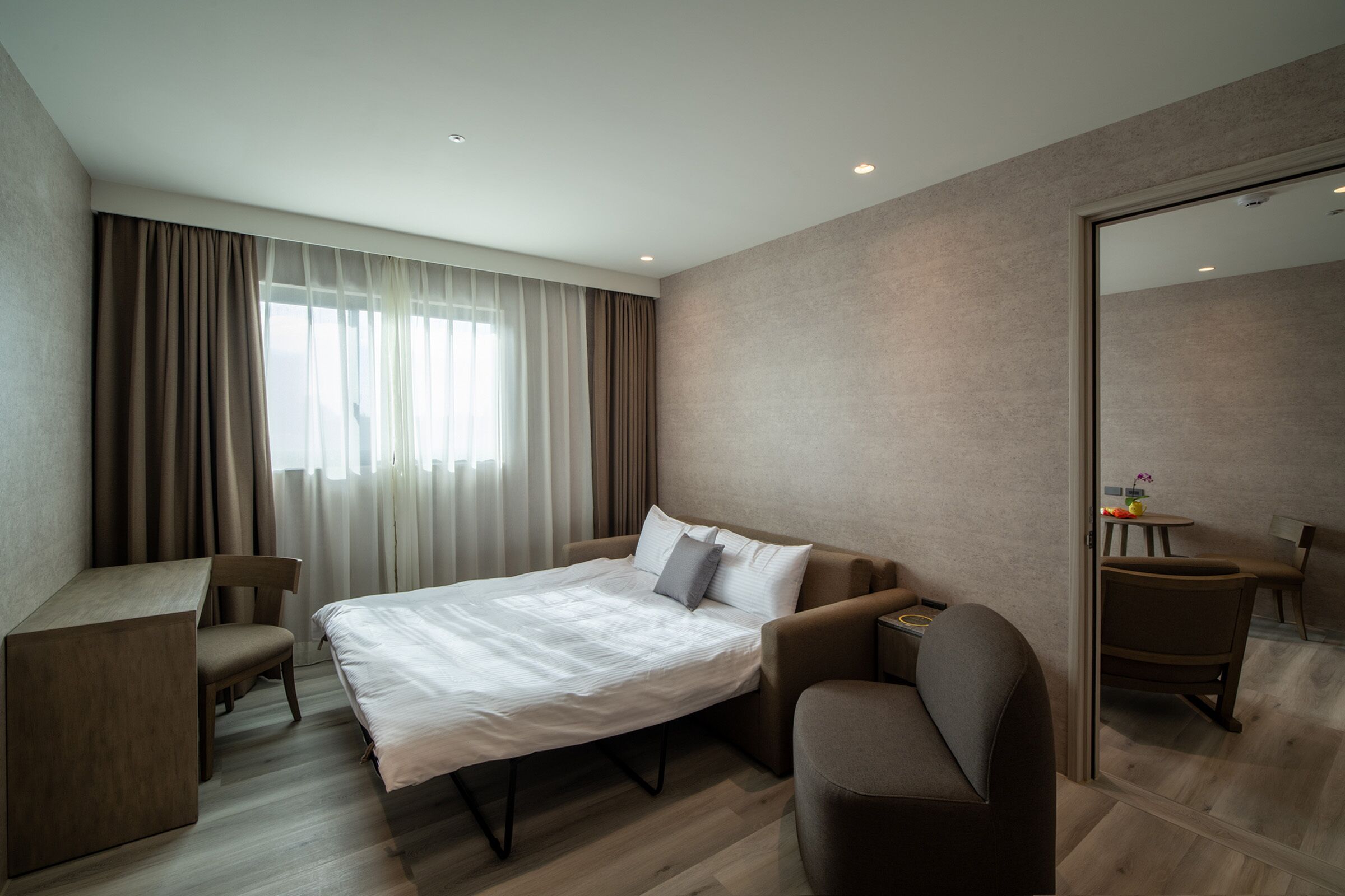 A modern hotel room with a large bed, a desk, and a seating area.