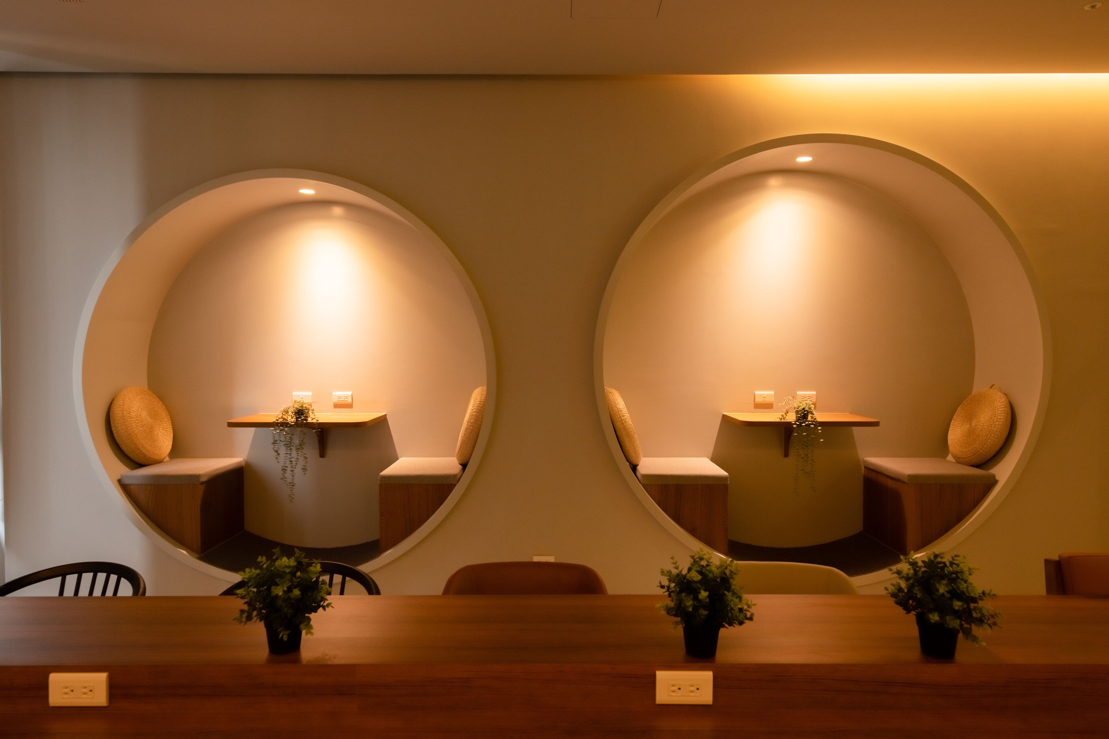 A conference room with a long wooden table, two circular wall niches with seating, and small potted plants.