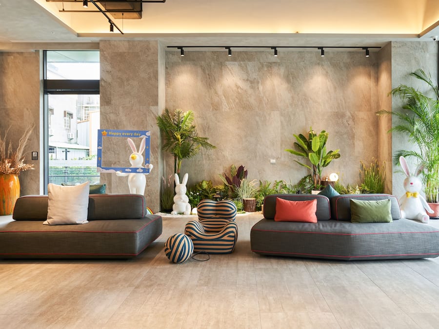A modern living room with a large window, a sofa set, a decorative rabbit sculpture, and various plants.