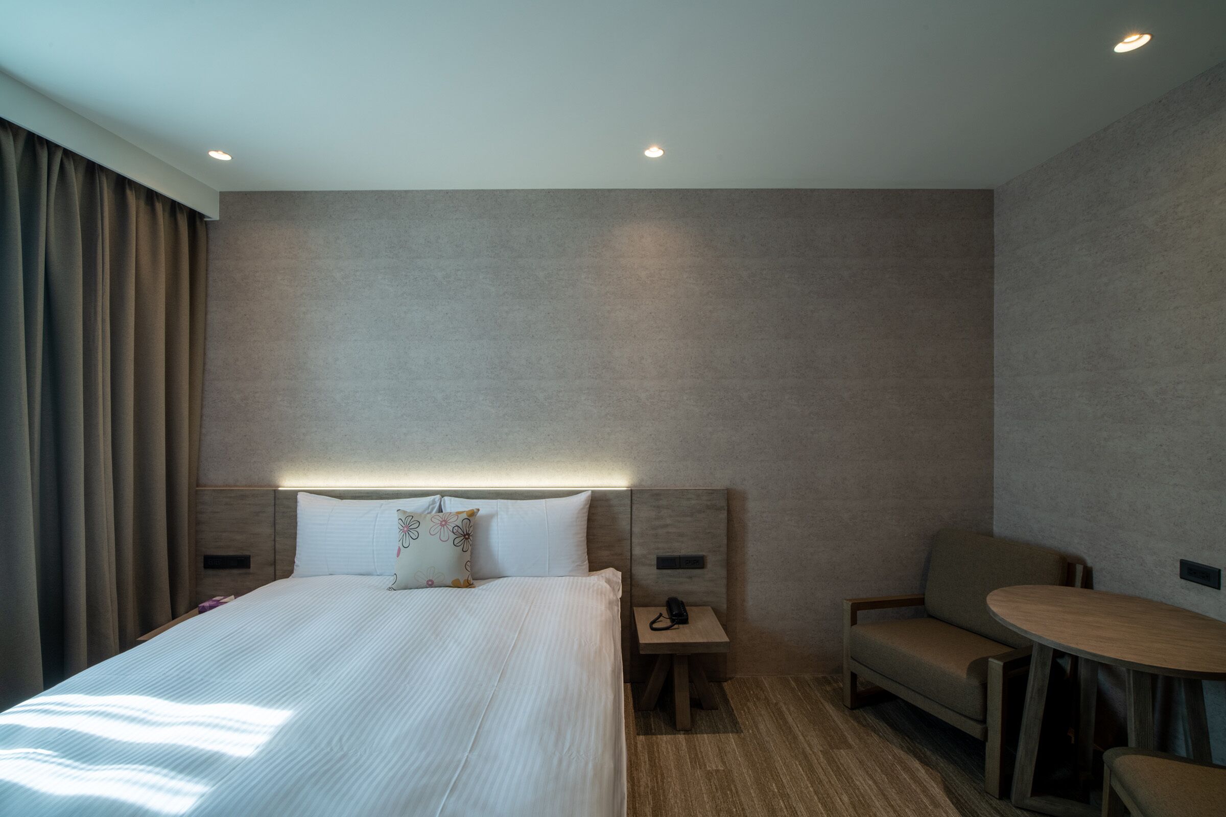 A modern hotel room with a large bed, bedside tables, a small sofa, and a round table.